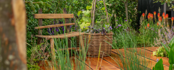 A rustic wooden bench sits on a timber decking that weaves naturally through the garden